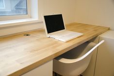 an open laptop computer sitting on top of a wooden desk next to a white chair