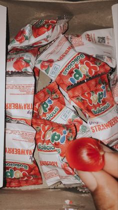 a box filled with lots of bags of candy sitting next to a hand holding an apple