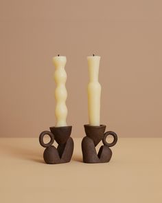 two candles sitting next to each other in front of a brown background with one candle on top of the other