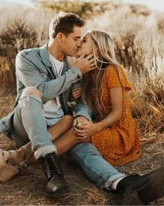 a man and woman sitting on the ground kissing each other in front of some dry grass