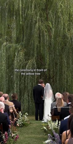 the ceremony in front of this willow tree is filled with people sitting down and looking at each other