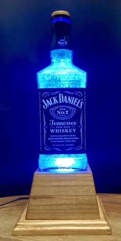 a bottle of jack daniels whiskey sitting on top of a wooden stand with a blue light behind it