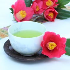 a cup of green tea next to some pink flowers