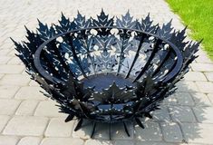 a black metal bowl sitting on top of a brick walkway next to grass and trees