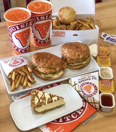 a table topped with two trays filled with sandwiches and french fries next to drinks