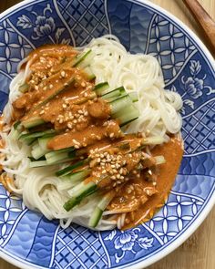 a blue and white bowl filled with noodles, sauce and veggies on top