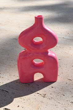 a pink vase sitting on top of a cement ground next to a shadow cast by the sun