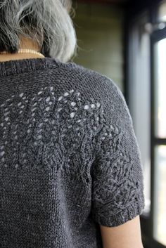 an older woman with grey hair wearing a gray knitted sweater looking out the window