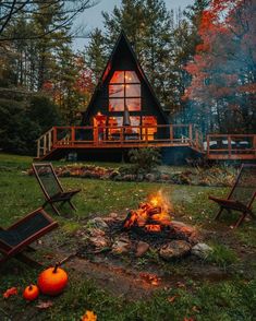 a cabin in the woods is lit up at night with pumpkins on the ground