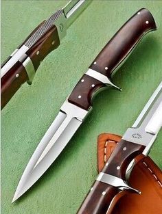 two knives are sitting next to each other on a green surface with leather sheaths