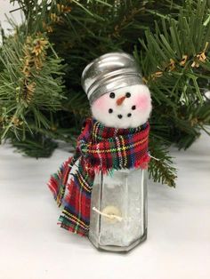 a small snowman in a plaid scarf and hat sitting on top of a lantern