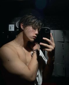 a shirtless man taking a selfie with his cell phone in the dark room