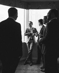 a group of men standing next to each other in front of a window with curtains