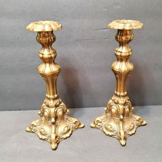 two gold colored candlesticks sitting next to each other on a gray surface,