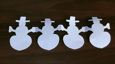 three snowmen cut out from paper on a table