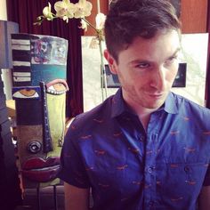 a man standing next to a vase with flowers in it and looking at the camera