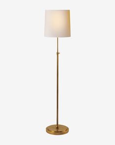 a floor lamp with a white shade on the base and a gold metal frame around it