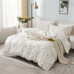 a white bed in a bedroom next to a window with flowers on the comforter