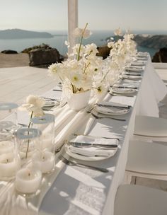 a long table with white flowers and candles on it is set for an outdoor dinner