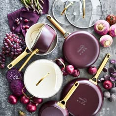 purple pots and pans with gold handles on a gray surface next to red onions