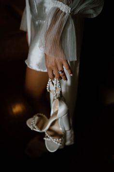 a close up of a person's hand holding a pair of white high heels