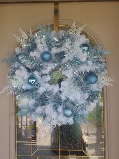 a wreath with blue and white ornaments hanging from it's front door, in front of a window