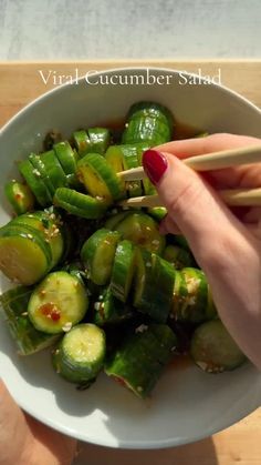 a person holding chopsticks over a bowl of food with green peppers and cucumbers