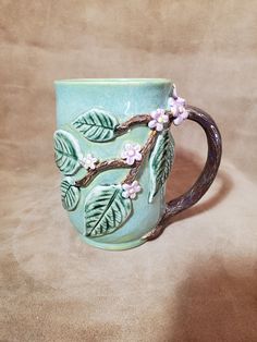 a ceramic mug with leaves and flowers painted on the inside is sitting on a tan surface