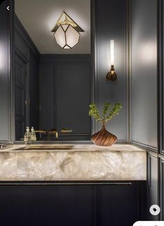 a bathroom with a marble counter top and two lights on the wall, along with a vase filled with flowers