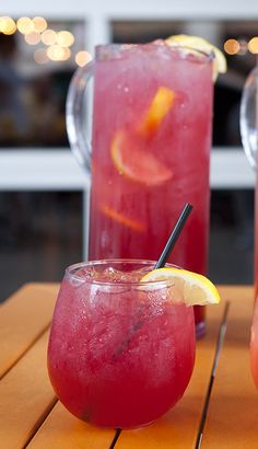 two glasses filled with drinks sitting on top of a wooden table next to each other