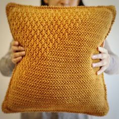 a woman holding up a pillow made out of yarn