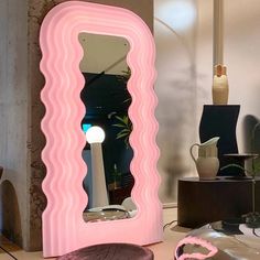 a large pink mirror sitting on top of a table next to a vase and lamp