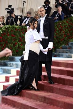 two people in formal wear standing on steps with cameras around them and one person wearing a tuxedo