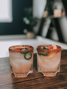 two glasses filled with drinks sitting on top of a wooden table next to each other