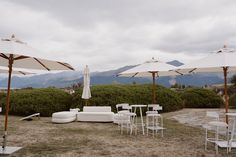 an outdoor seating area with umbrellas and chairs on the grass in front of mountains