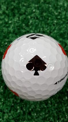 a white and red golf ball with a black ace on the side sitting on green grass