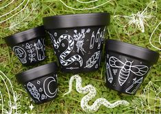 four black cups with drawings on them sitting in the grass next to some white string