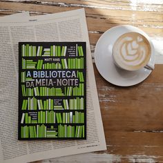 a book sitting on top of a wooden table next to a cup of cappuccino