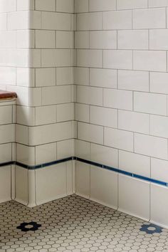 the corner of a bathroom with white tiles and blue lines on the floor, next to a urinal