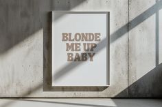 a sign that says blonde me up baby on it next to a concrete wall with the shadow of a window