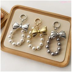 three charms with bows and pearls are on a tray next to a wooden container filled with beads