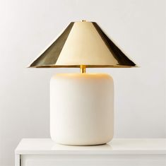 a white table lamp with a gold shade on it's top, sitting on a white surface