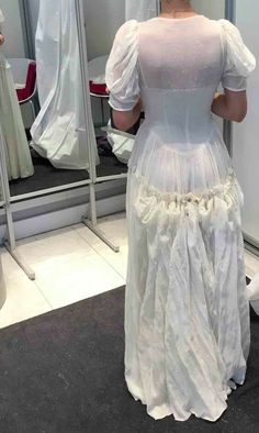 a woman in a white dress looking at herself in the mirror