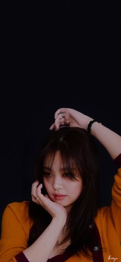 a woman with long dark hair wearing an orange shirt and holding her hand to her head