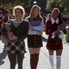 three girls in school uniforms are standing on the street