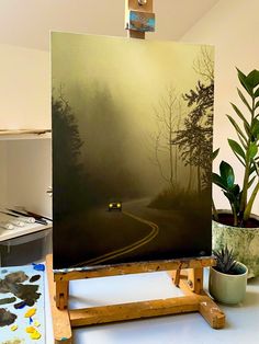 a painting is being displayed on a easel in front of a potted plant