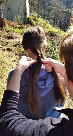 a man and woman sitting on the ground with their hair in a pony tail braid