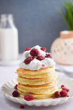 a stack of pancakes topped with whipped cream and raspberries on a white plate