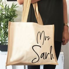 a woman holding a bag with the words mrs sahi on it and a plant in the background