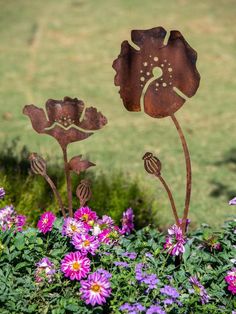 two metal flowers sitting in the middle of some purple flowers